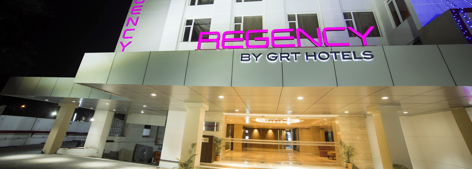 Regency GRT Hotels sign with purple letters and blue lights at night.
