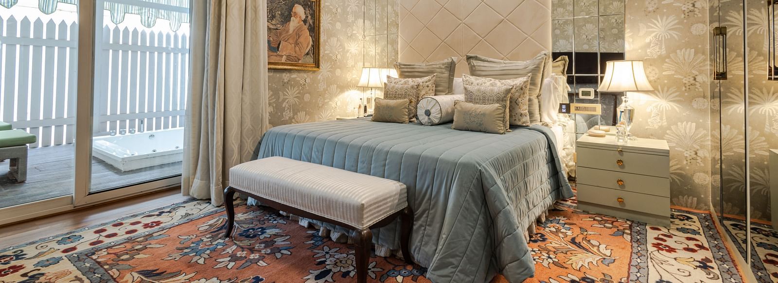 Luxury Suite with Whirlpool at The Claridges New Delhi, featuring a cosy bed with bedside lamps, a table at the foot of the bed, and a large window