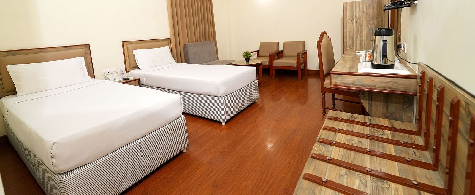 Hotel room featuring two single beds, a large flat-screen TV, and a comfortable seating area in Hyderabad near Ramoji Film City.