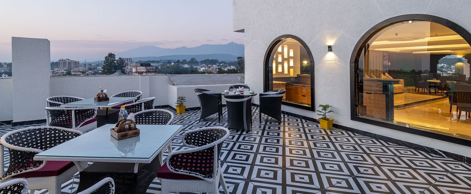 Image of rooftop restaurant Ruttba at DLS Grand Luxotica, Dehradun featuring dining setting on a well furnished floor with the scenic view of Dehradun city