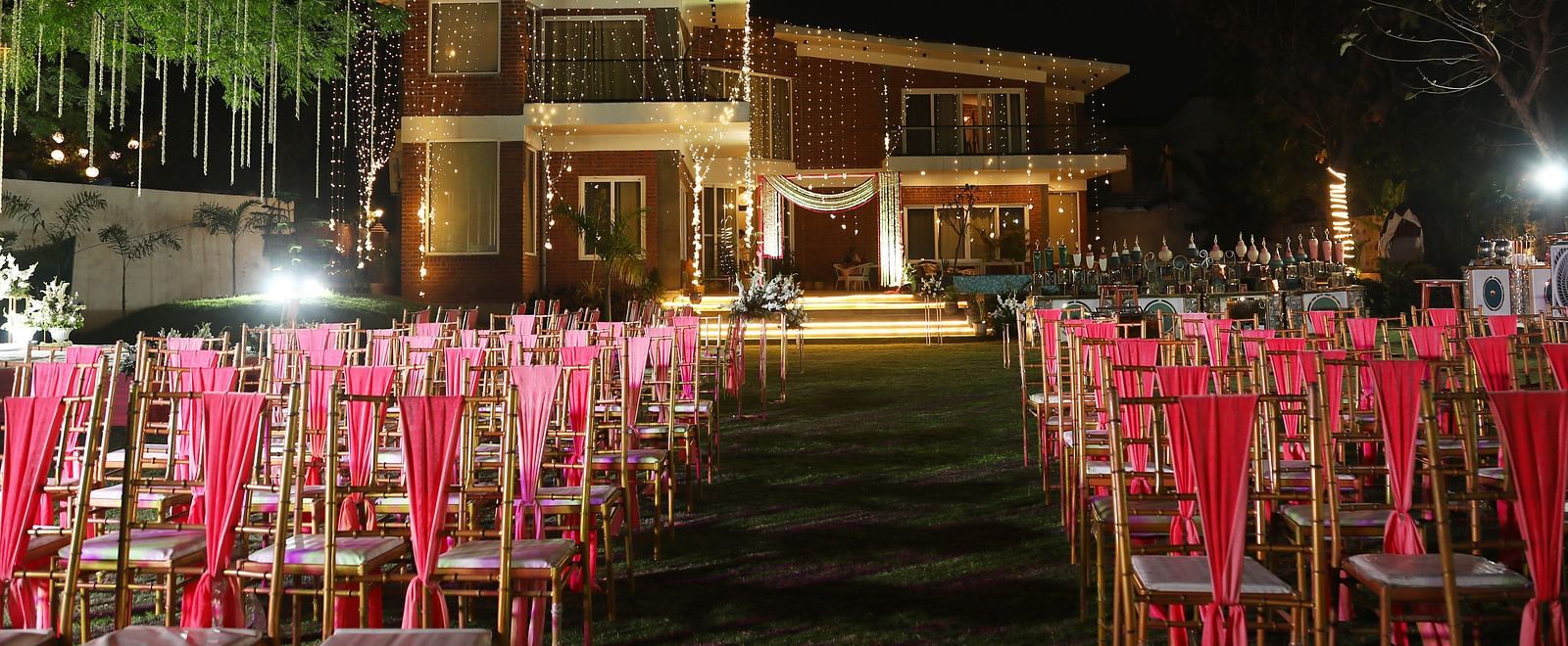 Outdoor event setup at Tisya Farms, Gurgaon with rows of red chairs facing the lit-up main building at night.
