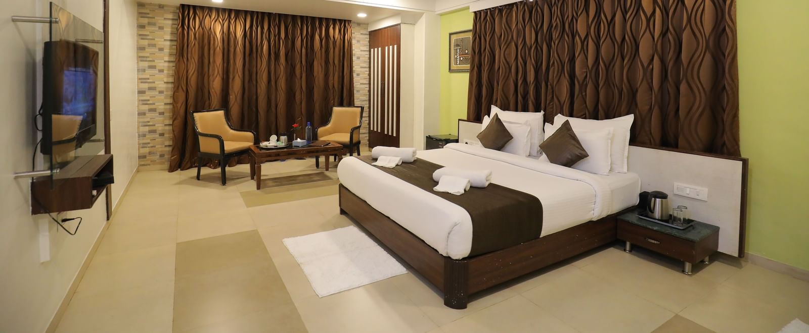 A spacious bedroom at Krushnai Resort featuring a king size bed, wall-mounted TV, and brown drapes.