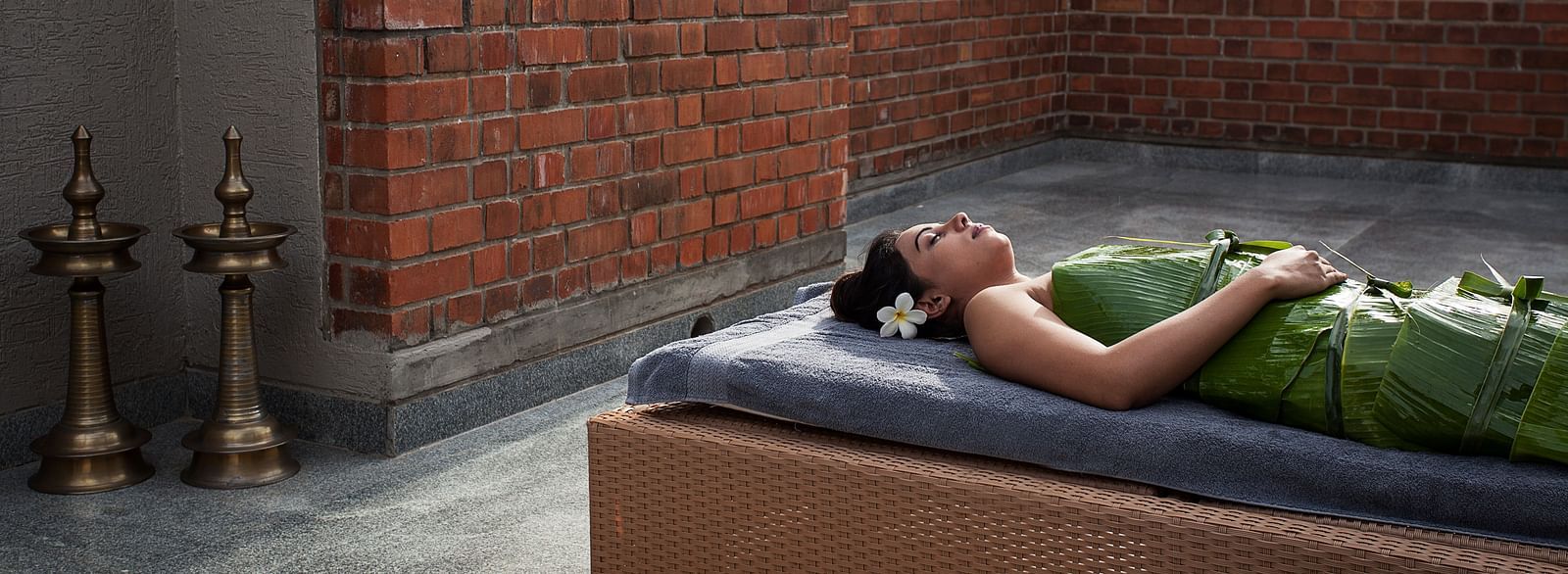 Person lying on a massage table outdoors, brick wall, spa treatment - Shreyas Retreat