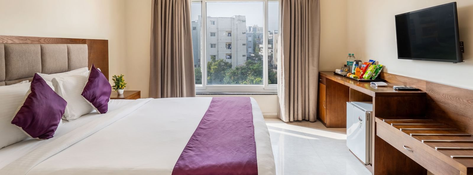 A well-lit room at Destino by Monday Hotels, Gachibowli, featuring a neatly made double bed, a wall-mounted TV, and wooden furnishings.
