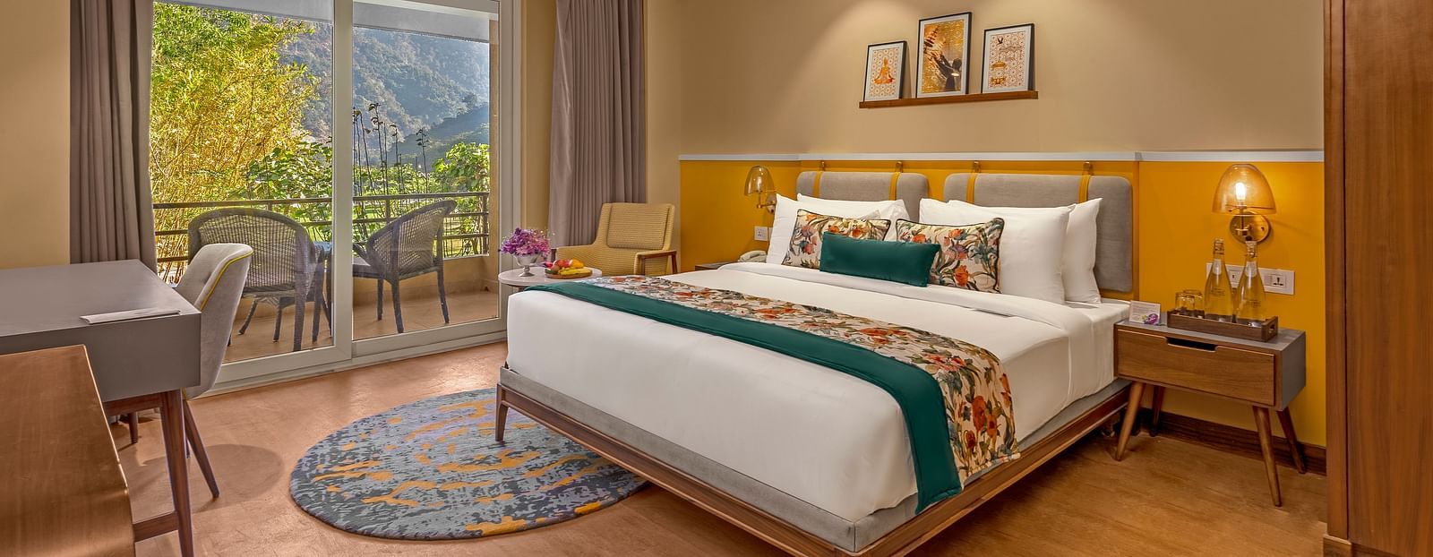 Image of a  room features a large king-size bed with a plush headboard and comfortable bedding. A comfortable armchair sits by a large window offering breathtaking views. The room also includes a wooden desk with a chair, a television, and a ceiling fan. T