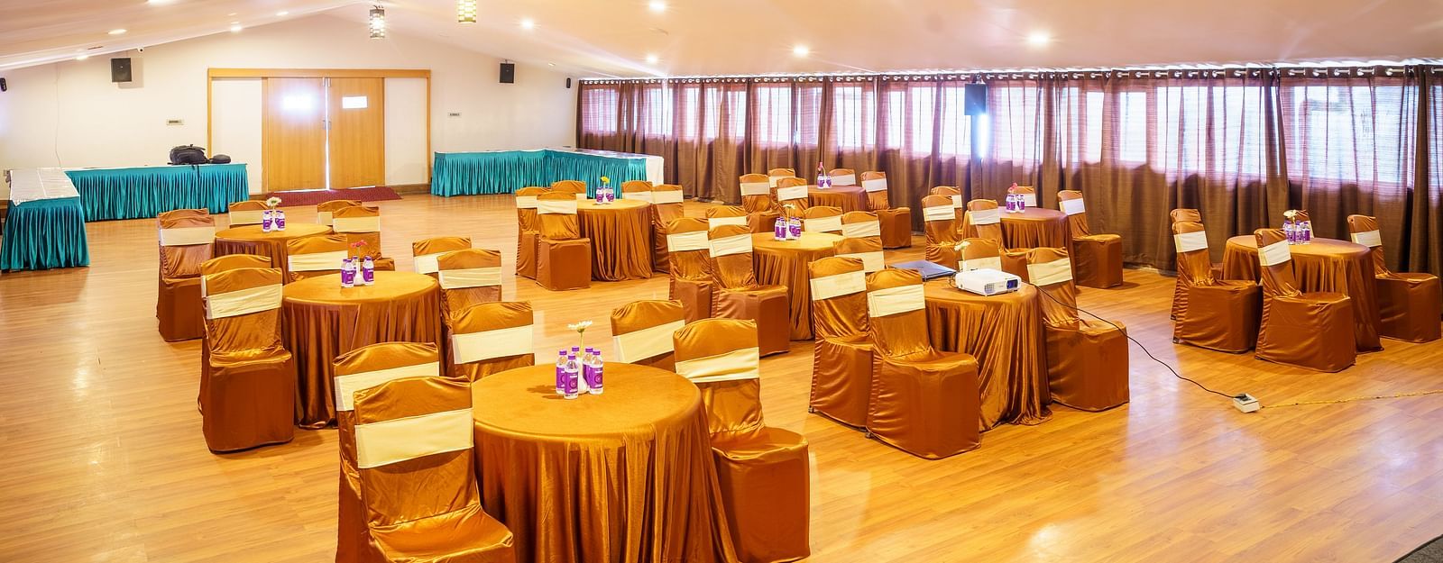 A spacious event hall at Orsino Hotel & Spa arranged with round tables draped in gold and matching chair covers, ready for a gathering.