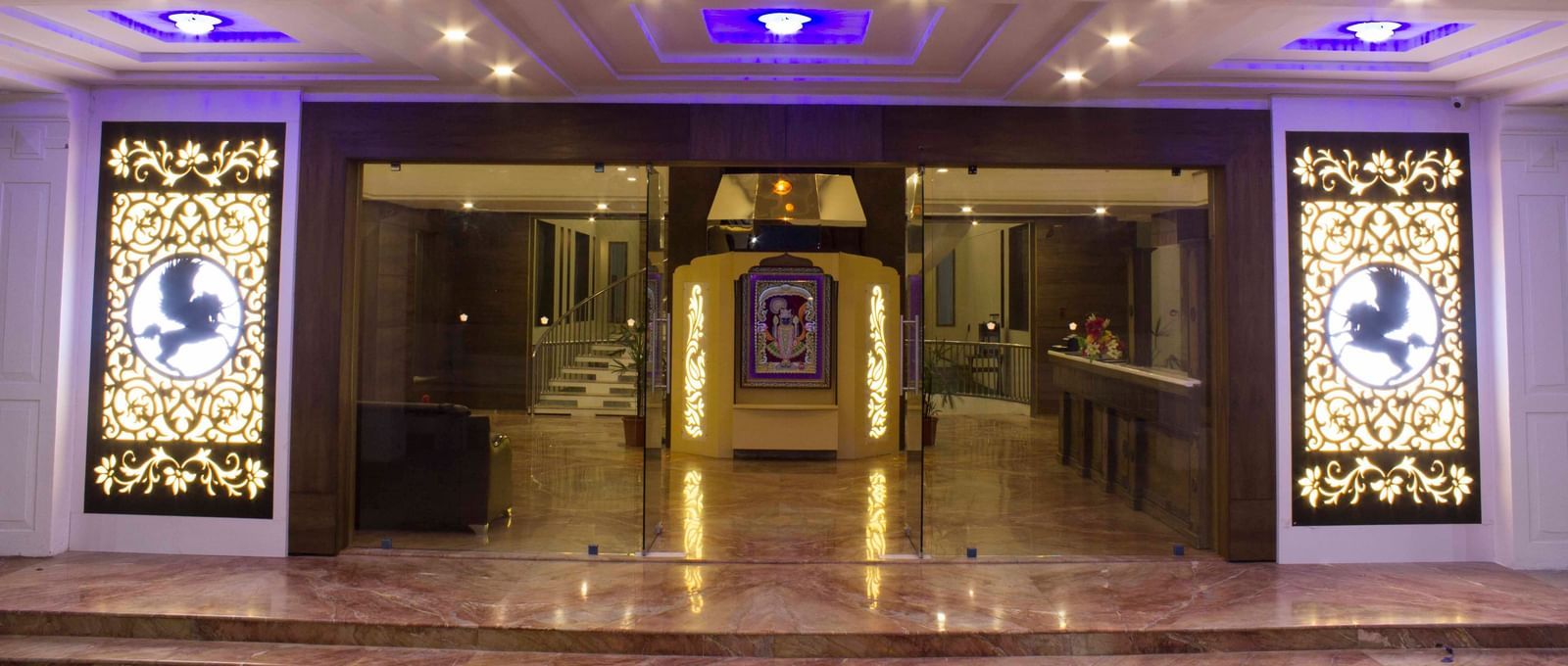 A hotel entrance with grand doors and blue-lit ceilings | Daksh The Madhuvan Suites