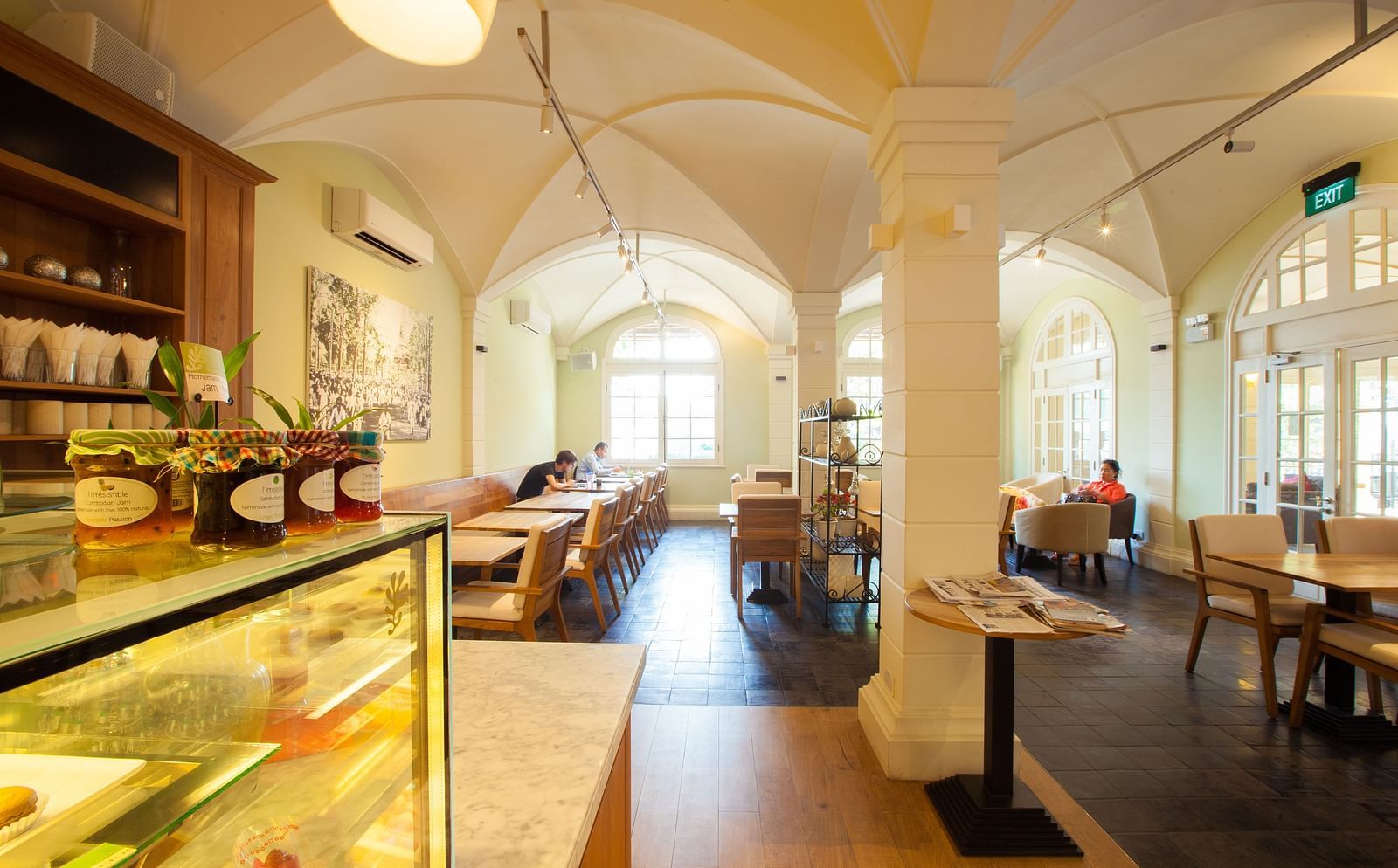 A cafe interior with tables and chairs, display shelves, and a long counter | The Shop | Central Mansions, Phnom Penh
