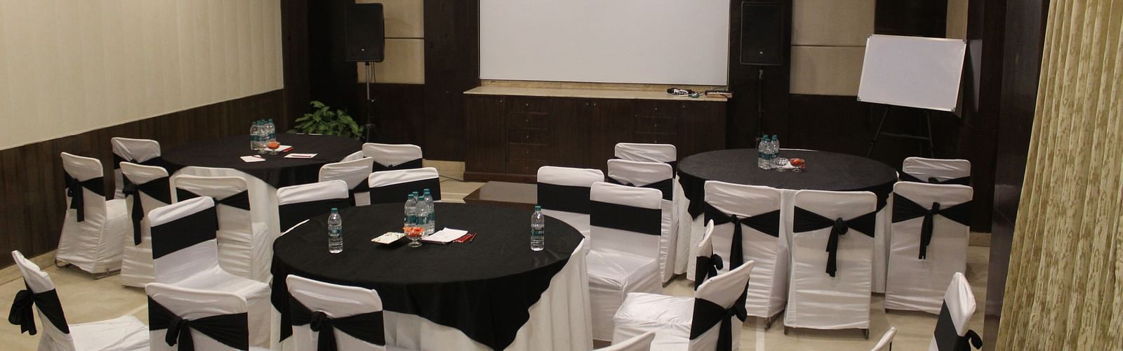 An image of a banquet hall  featuring a few round tables, each surrounded by chairs at Inde Hotel Signature Tower, Gurgaon