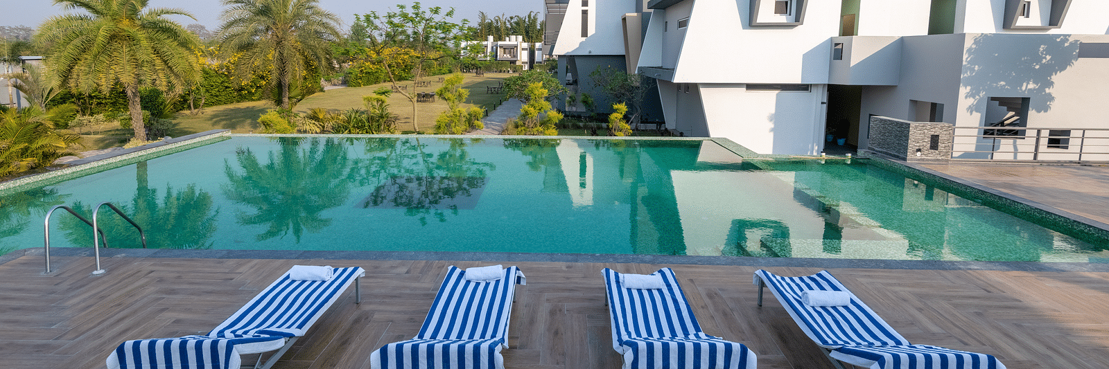 Pool area with lounge chairs placed beside it, offering a view of trees on one side at DLS Forest Vines Resort.
