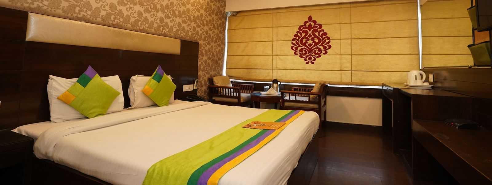 Low angle view of Deluxe room with king-size bed, two chairs with centre table at Hotel Dreamland, Chandigarh.