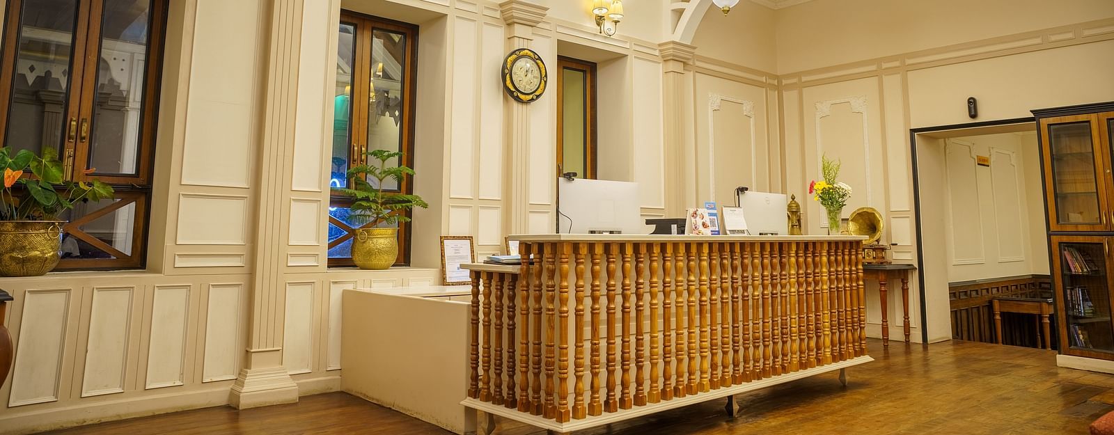 A warmly lit reception area  of Orisino Hotel & Spa that features a wooden front desk, ornate chandeliers, and large windows