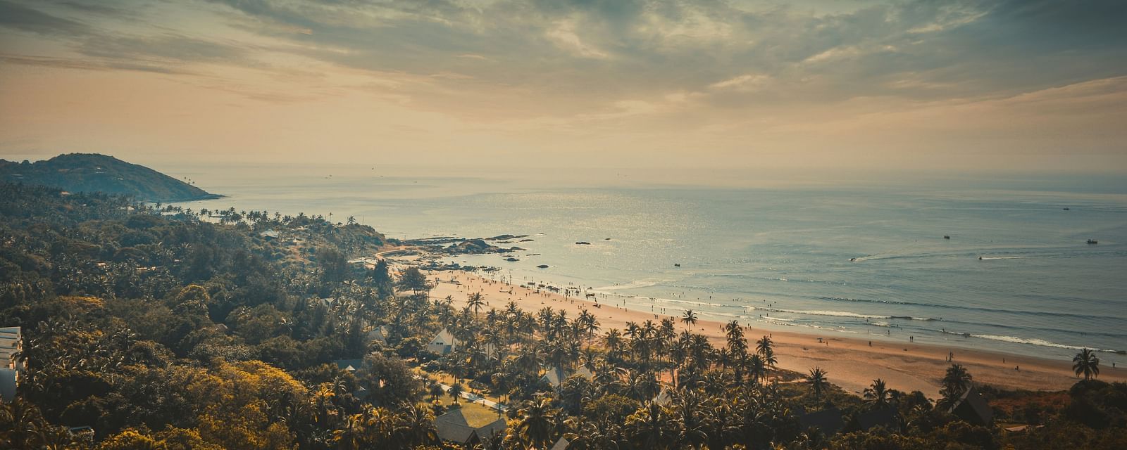 Panoramic view of a sandy beach with palm trees and a dramatic sky at sunset.