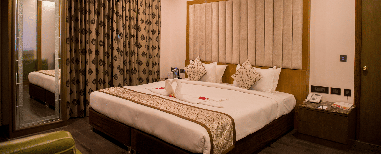 A hotel room at Benzz Park Chennai featuring a neatly made bed with white linens, a bedside table, and curtains.