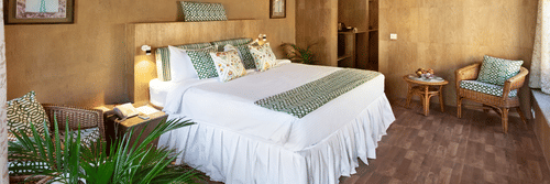 An attic style bedroom featuring double size bed, a bedside table, flower pots, and a seating area at Suryavilas Luxury Resort and Spa