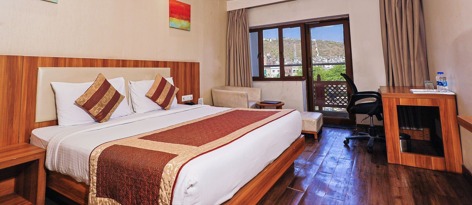 A low angle view of the bedroom with comfy bed and balcony, table and fan at Le Roi Udaipur