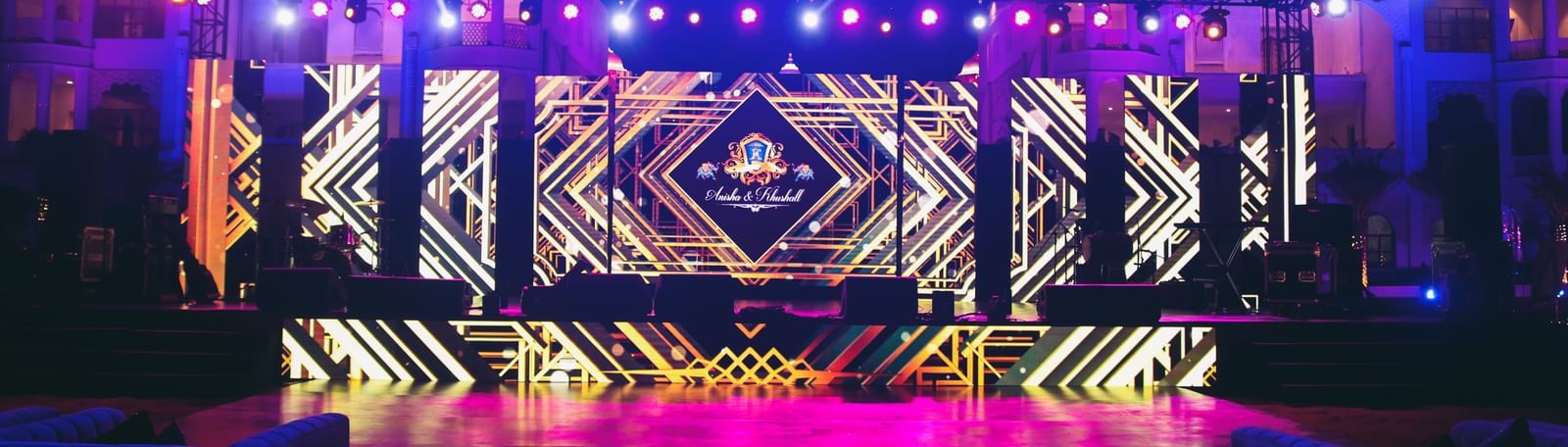 A stage set against the towering Kaldan Samudhra Palace, for celebrating the wedding of Anisha & Kushaal featuring large speakers, spotlights hanging from the top and a large screen