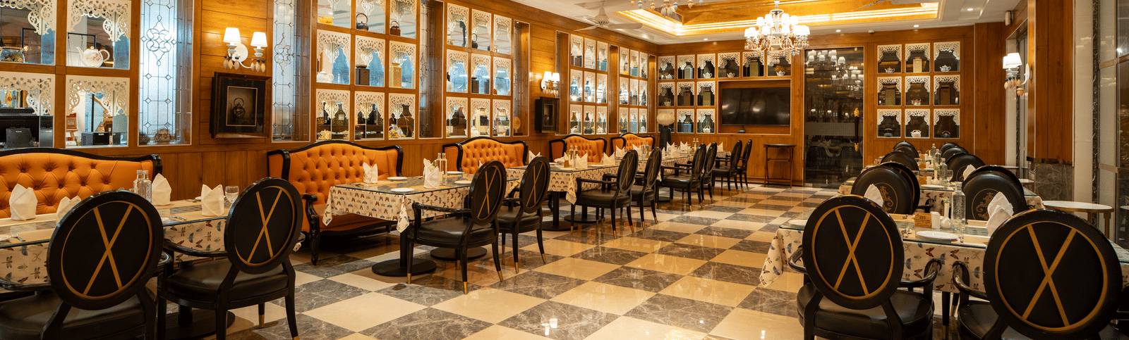 An elegant, formal dining room or restaurant with ornate chandeliers, dark wooden paneling, and a stylish black and white diamond-patterned floor.