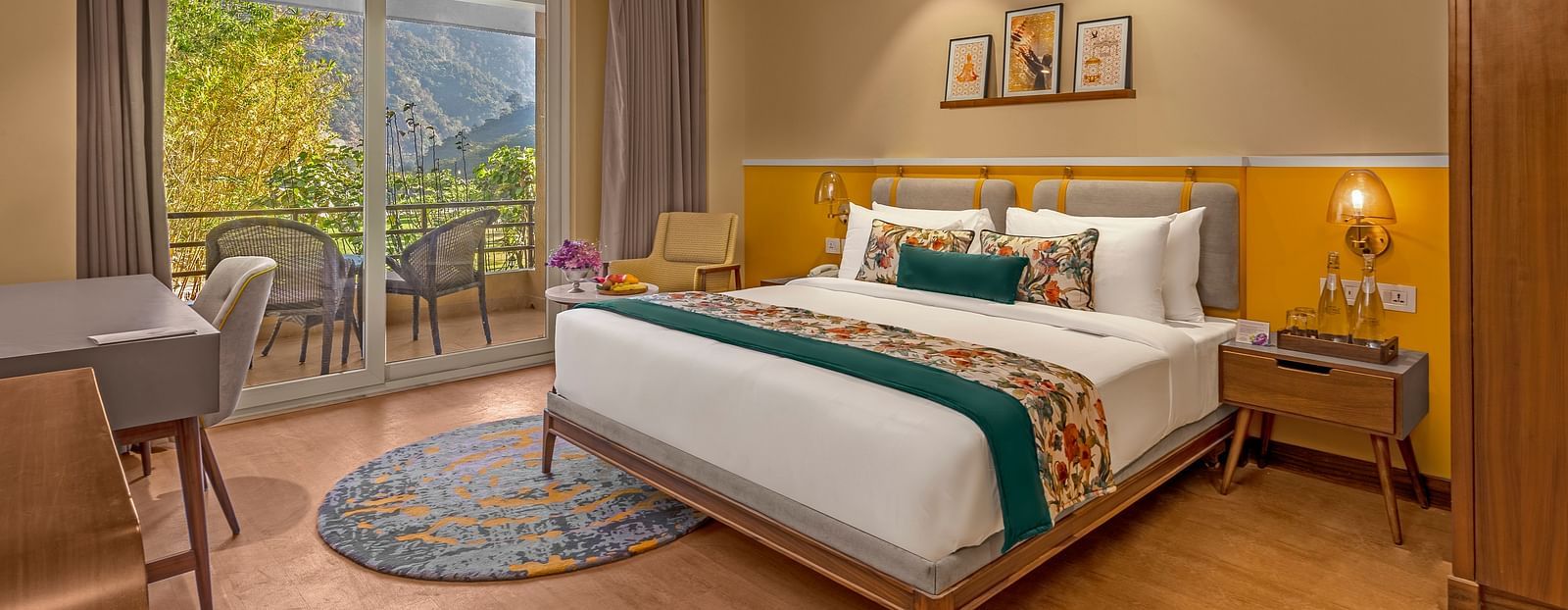 Image of a  room features a large king-size bed with a plush headboard and comfortable bedding. A comfortable armchair sits by a large window offering breathtaking views. The room also includes a wooden desk with a chair, a television, and a ceiling fan. T