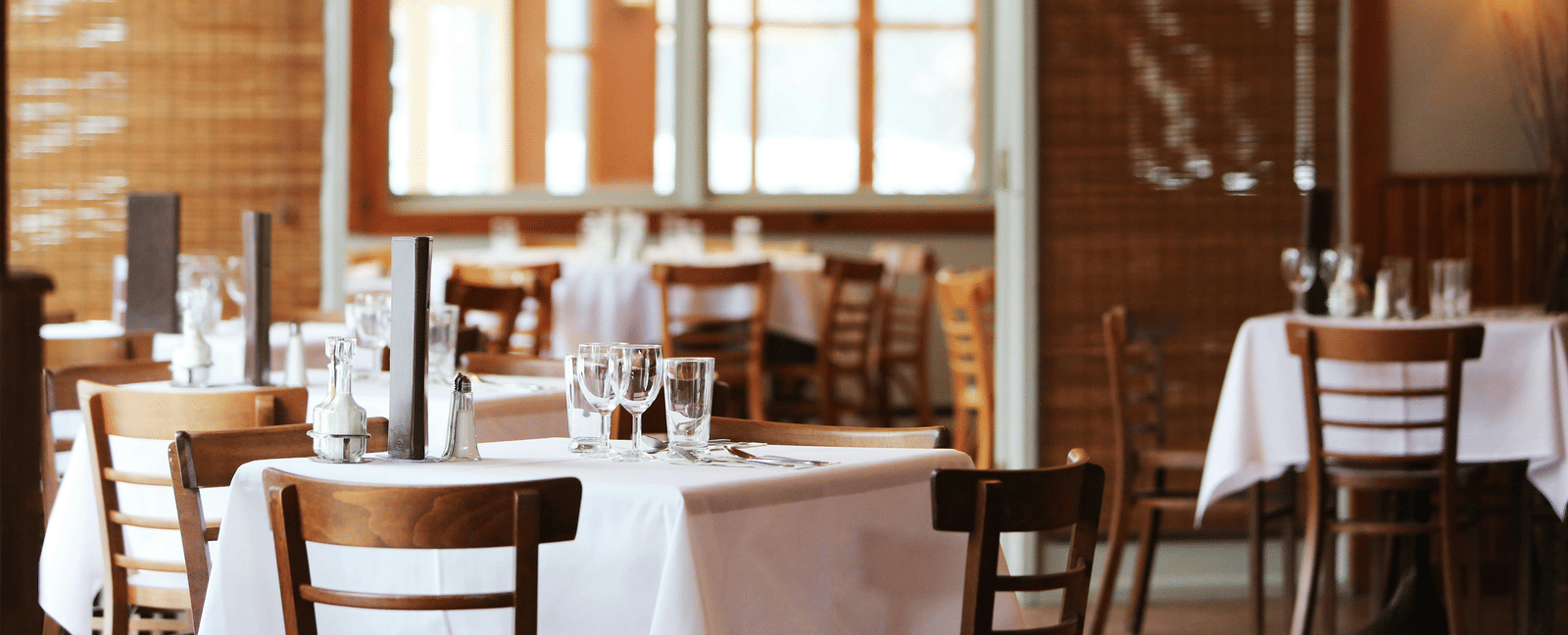 Elegant restaurant interior with neatly set tables, wooden chairs, and soft ambient lighting.