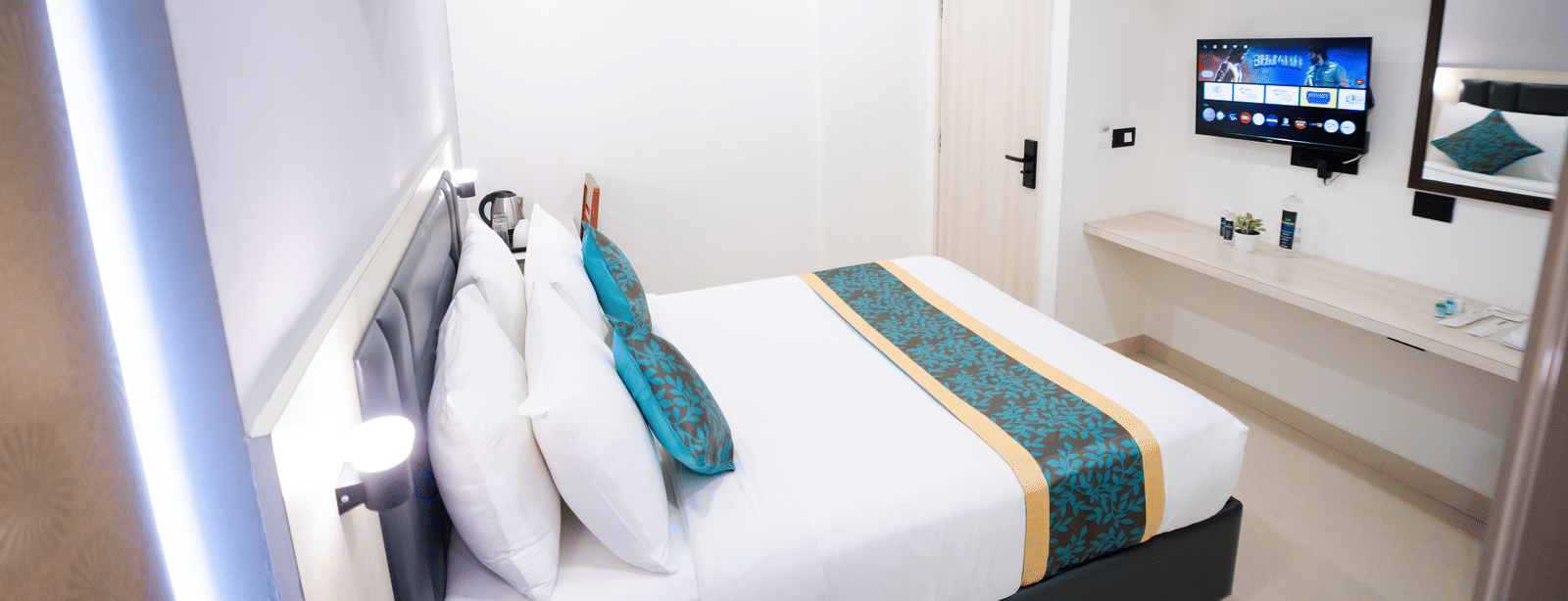 View of a large bed, wall-mounted TV, and mirror at Sunrise Business Hotel, Hyderabad.