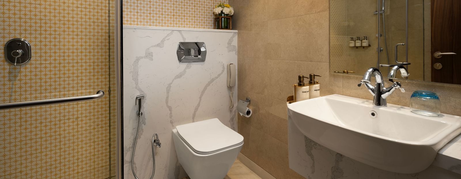 An image of a modern bathroom with a toilet, sink, and shower. The walls are tiled and there is a large mirror above the sink.