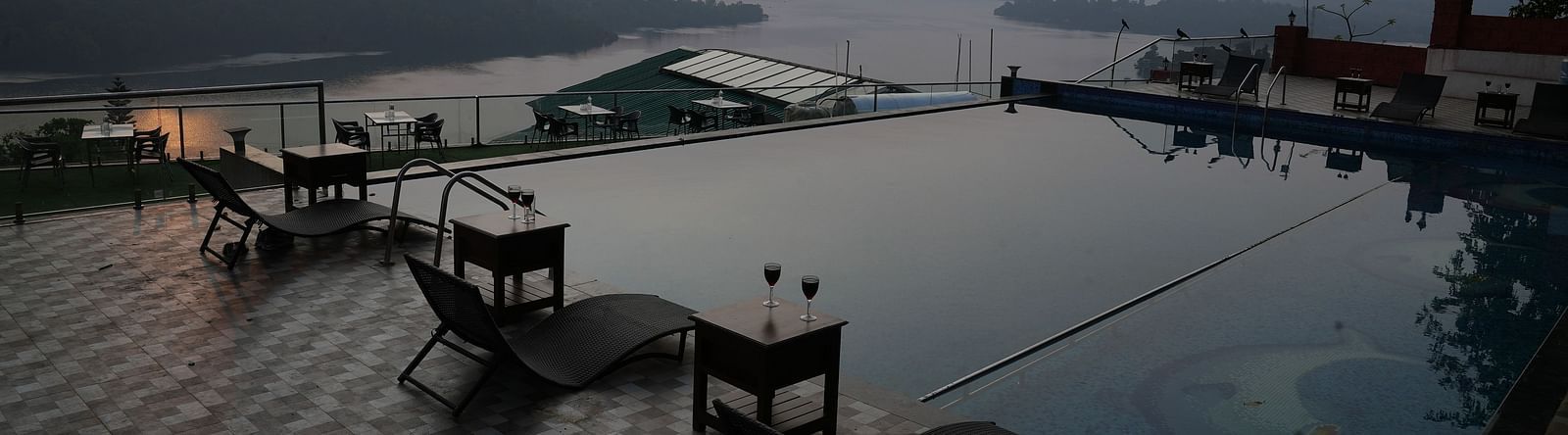 An image of the infinity waterfall swimming pool with lounge chairs placed beside it - Nisarga Lake Resort
