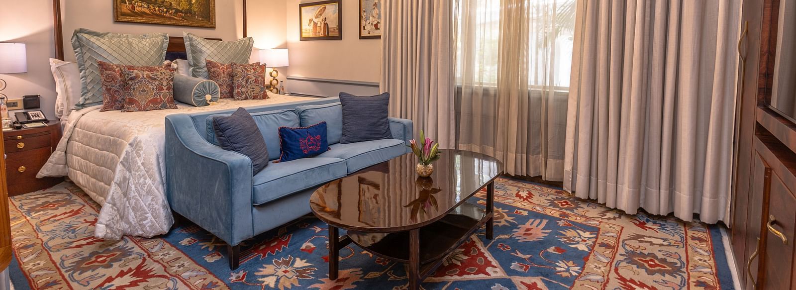 image of the brightly lit bedroom with a king size bed and blue couch place in front of the bed at our heritage parlour suites - The Claridges New Delhi