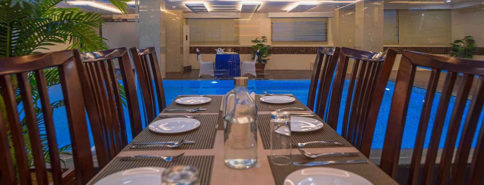 Dining table setup with plates, glasses, and cutlery near the pool at Mansha Regency, Port Blair.