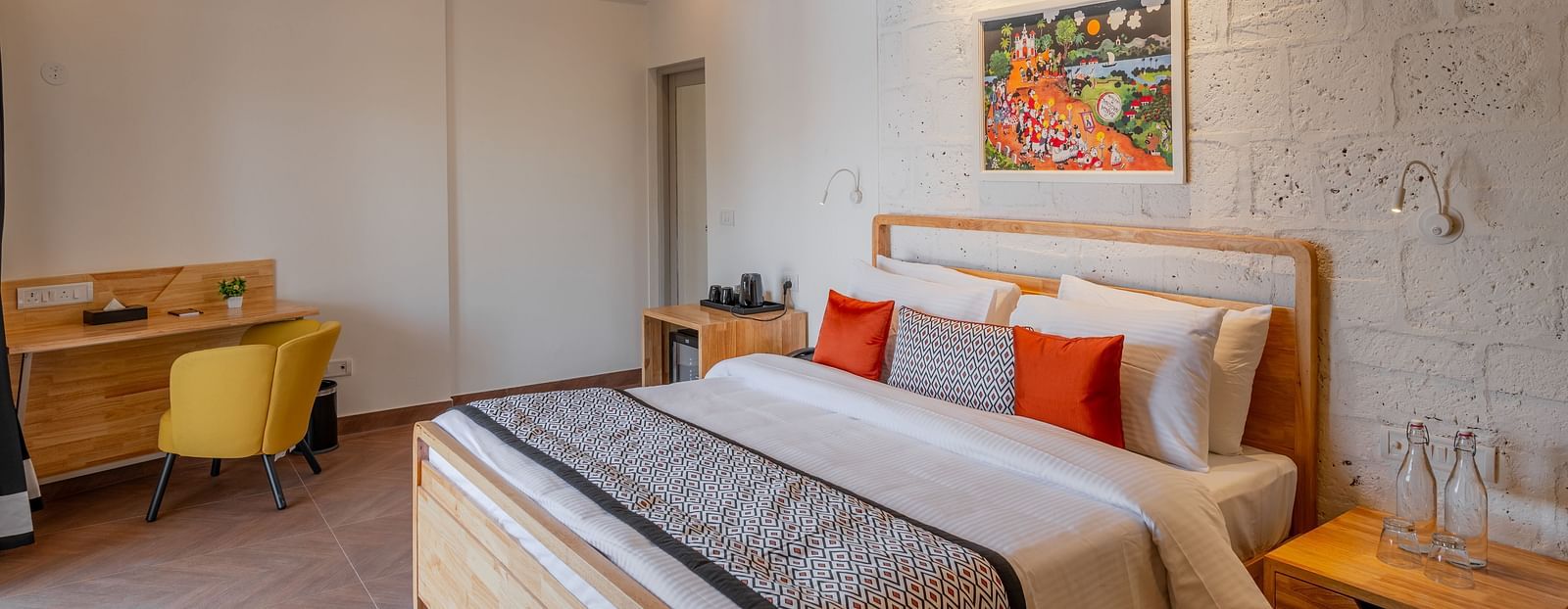 An image of hotel room with king size bed, painting on the wall, work desk and chair at one corner and a bedside table  at Bedzzz Xclusiv Morjim, Goa