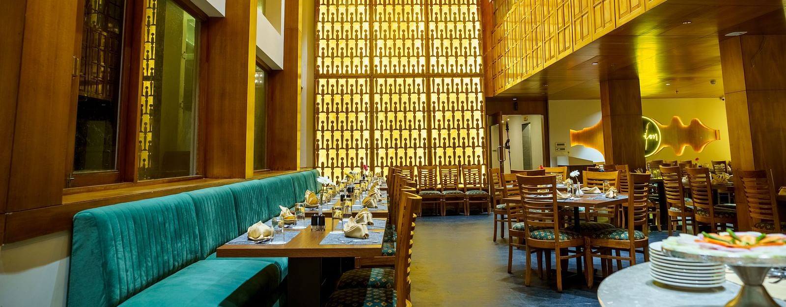 A warmly lit restaurant at Orsino Hotel & Spa features wooden walls, varied seating including a teal banquette, and set tables.