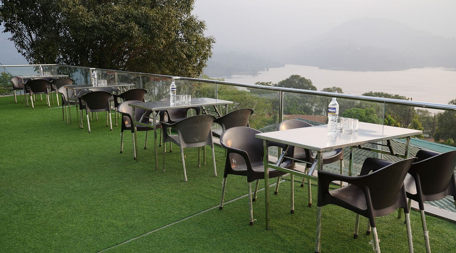 An image of the Lake View Oasis restaurant with chairs and tables at the rooftop and mountains and lake view in the background - Nisarga Lake Resort