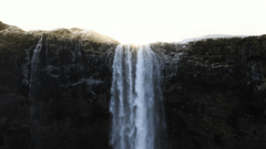 Waterfall cascading down a cliff with sunlight shining through.