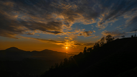 A silhouetted view of a valley with the sun setting in the background.
