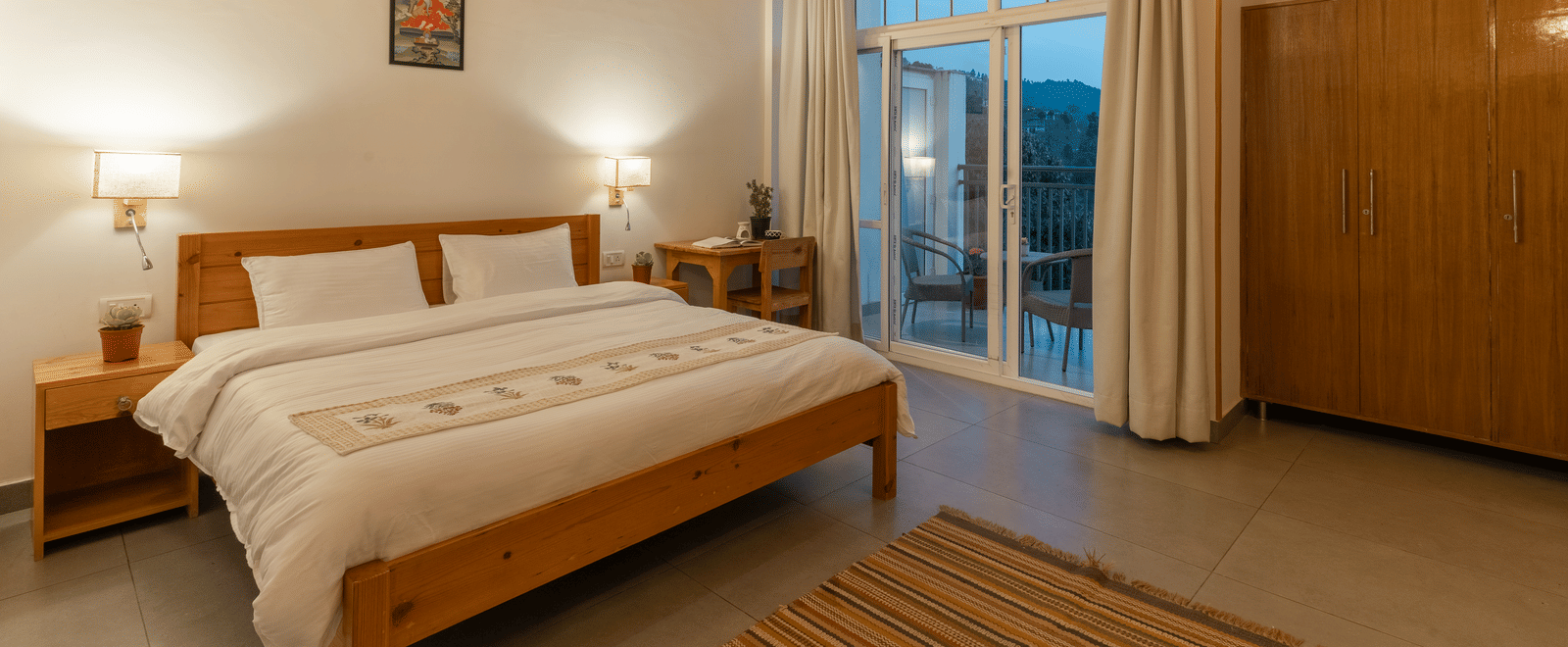 A bedroom at Ziran Retreat with a large bed, wooden furniture, and a floor-to-ceiling window looking out at a scenic view.