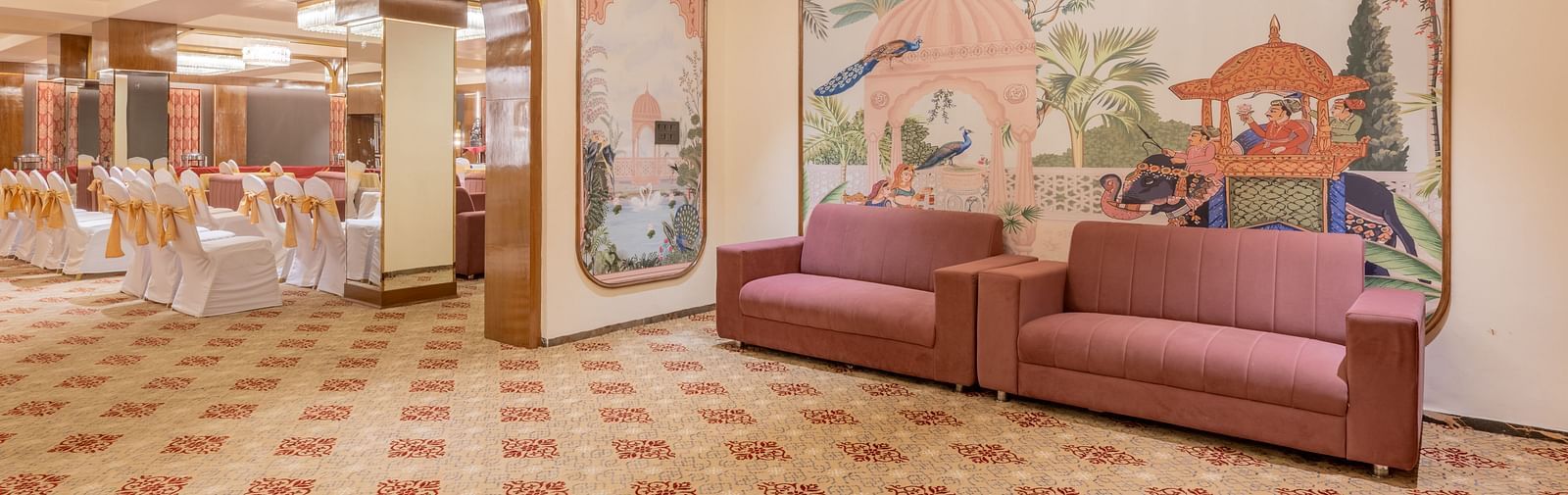 Spacious hall featuring maroon sofas and traditional mural paintings on the wall, visible from the banquet area at Hotel Highway King, Jaipur.