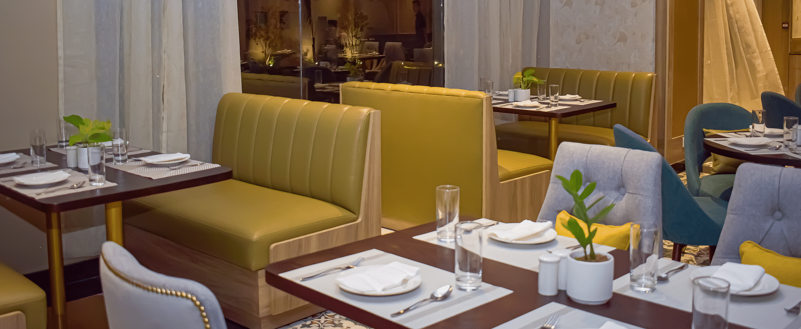 A restaurant interior with booth seating, set tables, sheer curtains, and hanging pendant lights - Urban Suites by BluSalzz, Jaipur