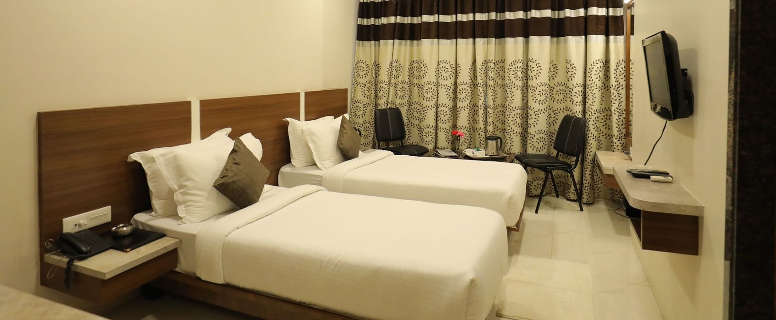 Side view of the Super Deluxe Rooms that are furnished with twin beds, wall-mounted TV, a seating area for two, and drawn curtains at Highland Resort.