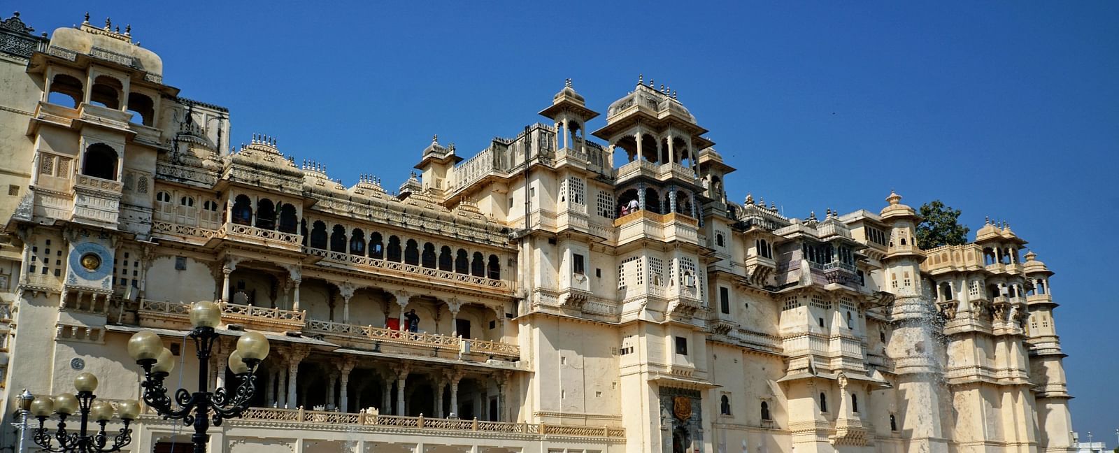 Facade view of City Palace in Udaipur with a garden and people in front of it.