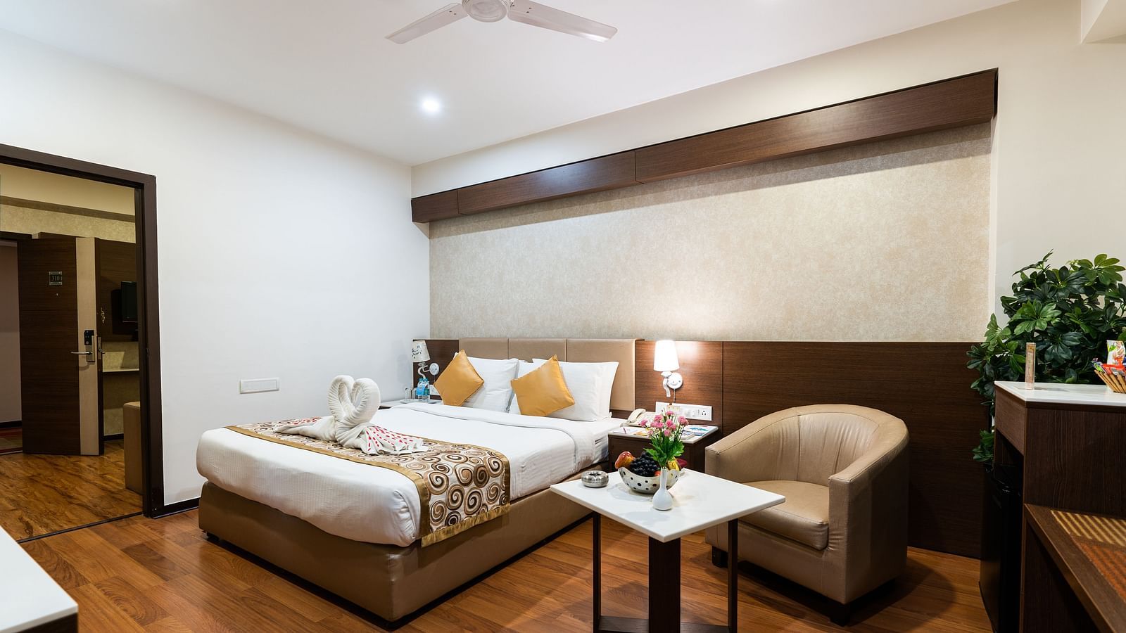 a double bed with a single seater sofa and a table next to it inside one of the rooms - Hotel Pai Vista, Mysore
