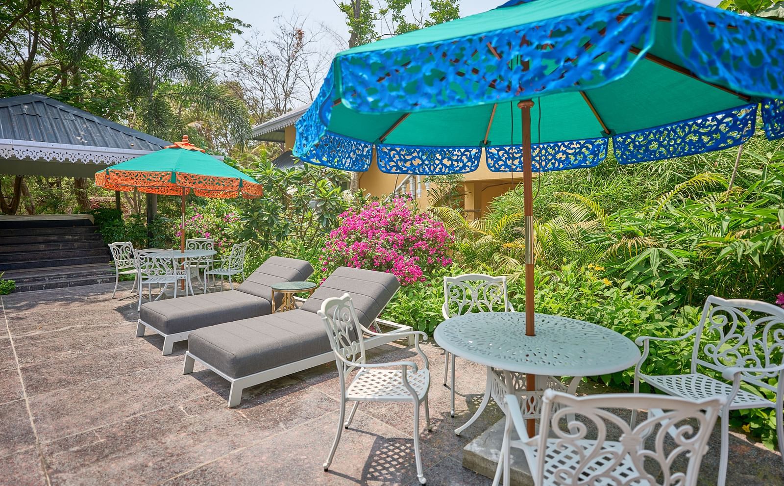 Lounger chairs and an umbrella placed over the table, with plants and trees in the background at Mayfair Manor, Alibag