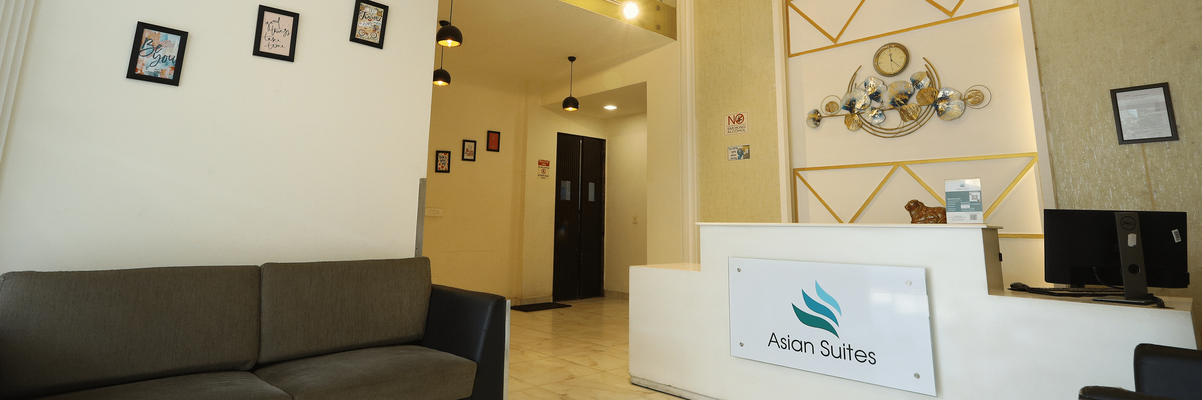 A brightly lit hotel lobby with a modern design, including a reception desk, comfortable sofa, and artwork on the walls - Asian Suites Cyber Park, Gurgaon.