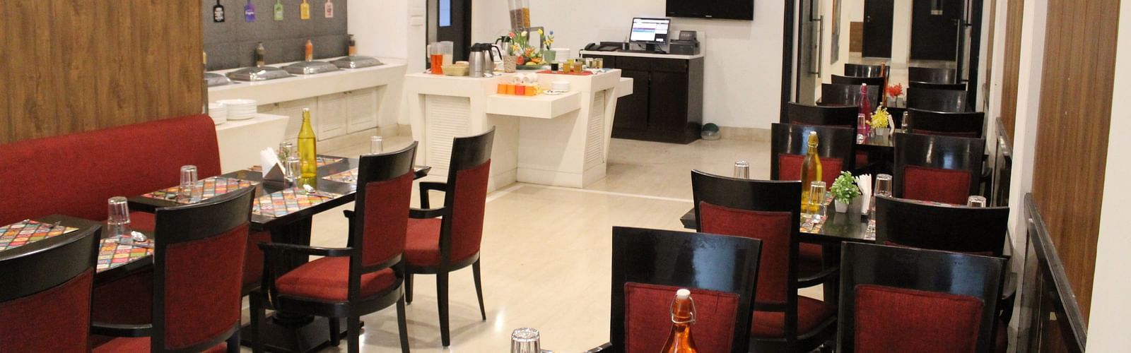 An image of a restaurant several sets of chairs and table where plates, cutlery, napkin, water bottles and other items are kept - Inde Hotels Vista Woods