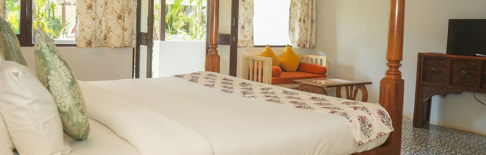Side view of a canopy bed near large windows overlooking greenery at De Soul Santé, Morjim.
