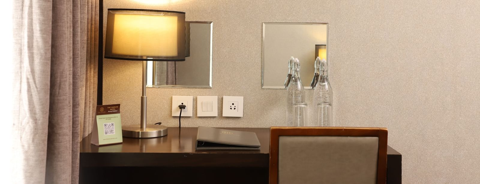 A workstation with a table lamp, sockets, and water bottles at The Hamuse Hotel, Kodaikanal