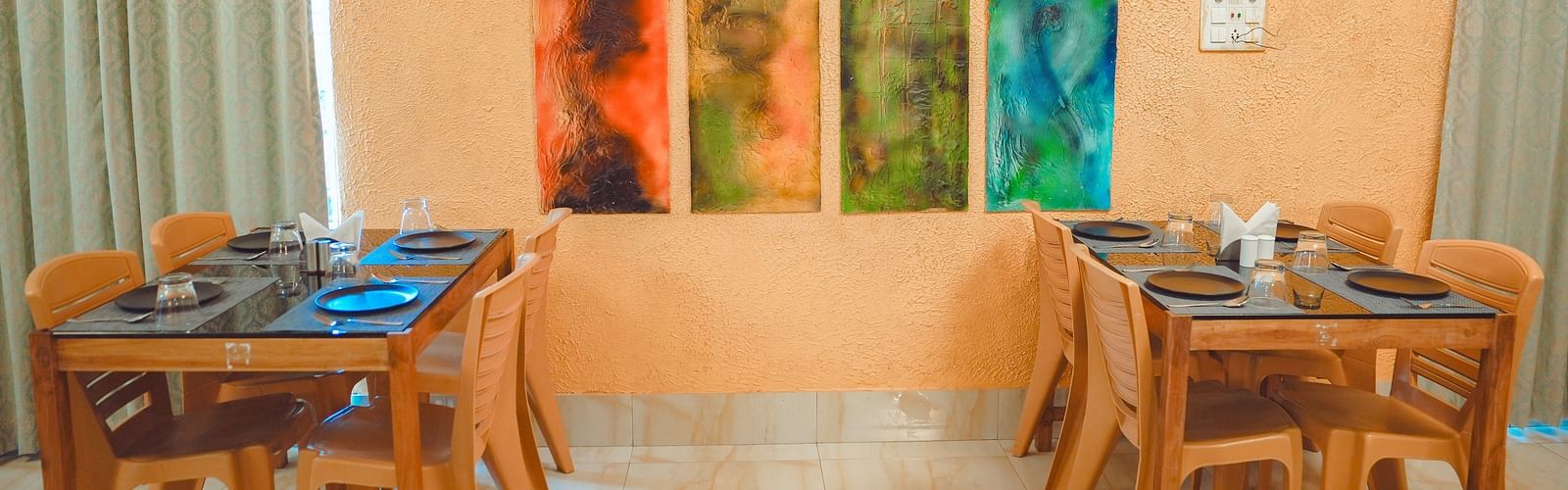 image featuring a series of wall mounted painitngs with dining tables on either side of it at mache vate banagali - Dip Holidays, Birbhum