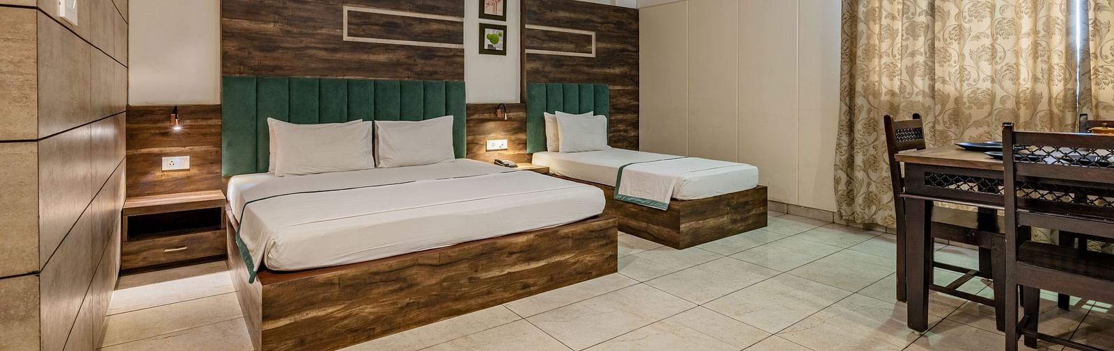 Extended view of the double and single bed, dining table and drawn curtains in the Suite of Hotel Highway King in Behror.