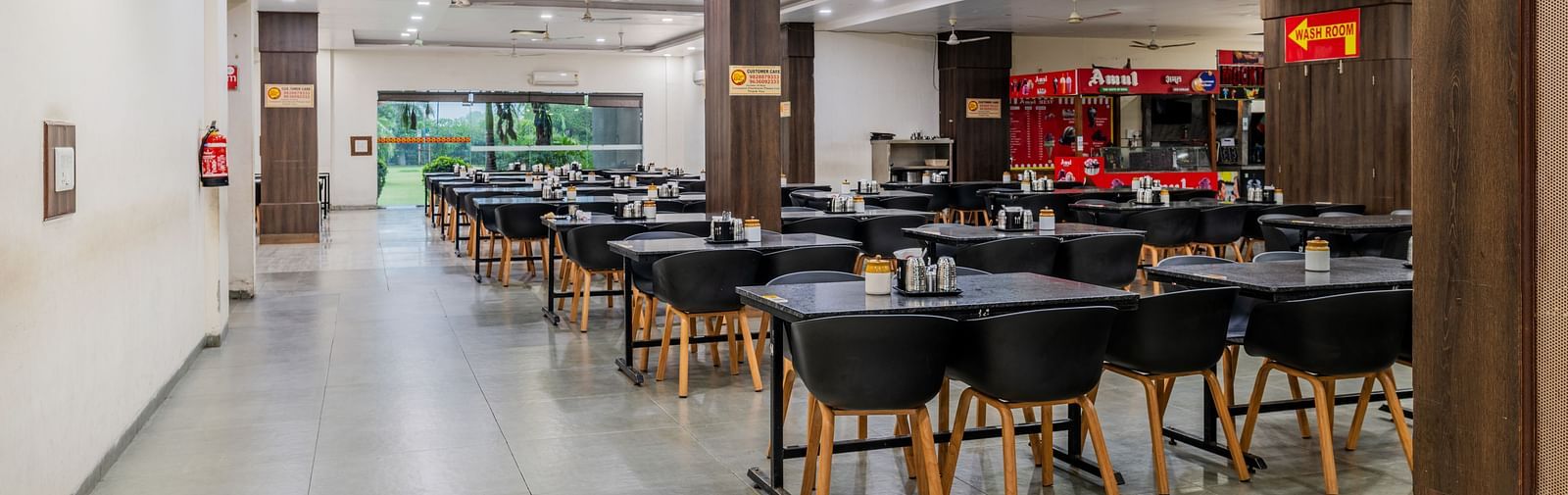 Dining tables with various seating capacities, ample lighting and eatery stalls located inside the restaurant of Hotel Highway King, Behror.