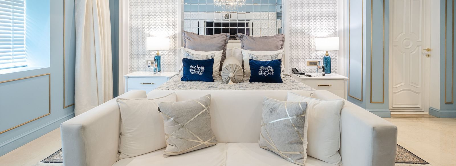 Claridges Suite at The Claridges New Delhi, highlighting the front view of a plush bed flanked by bedside lamps and illuminated by a chandelier overhead