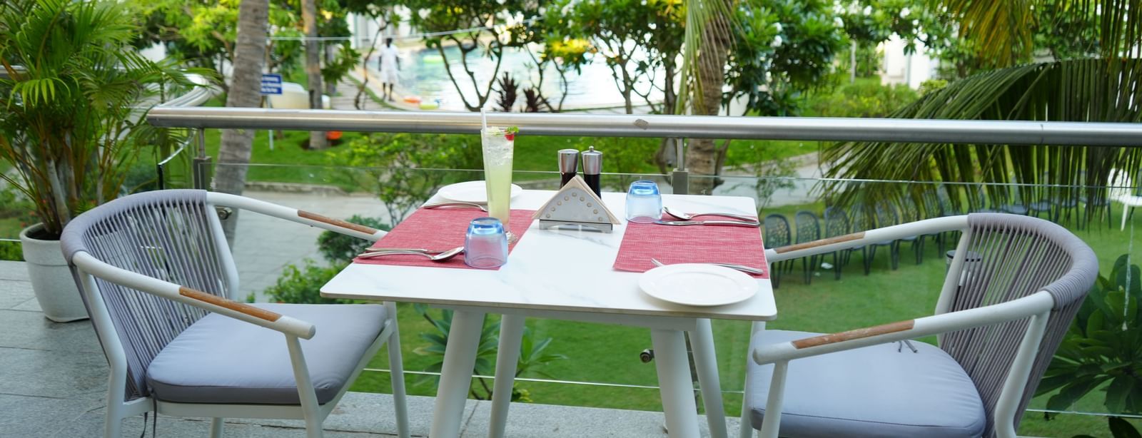 An outdoor dining table with two chairs placed beside palm trees at Grande Bay Resort & Spa.